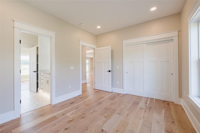 unfurnished bedroom with ensuite bathroom, light wood-type flooring, and a closet