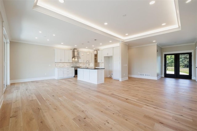 unfurnished living room featuring french doors, ornamental molding, a tray ceiling, and light wood-type flooring