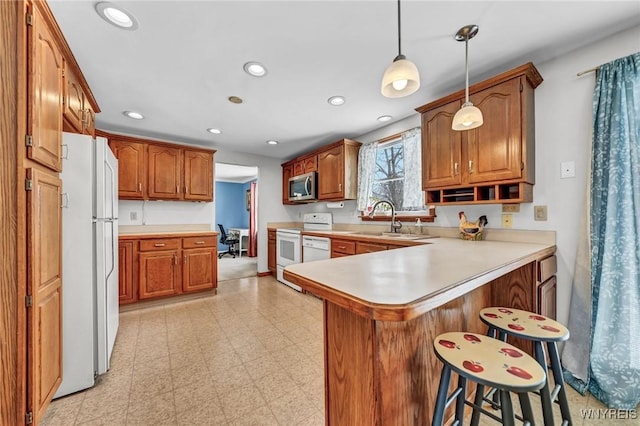 kitchen featuring white appliances, a kitchen breakfast bar, built in desk, decorative light fixtures, and kitchen peninsula