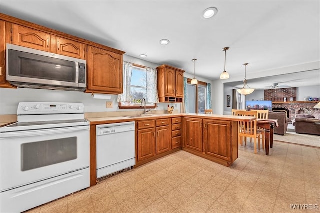 kitchen featuring pendant lighting, sink, kitchen peninsula, a brick fireplace, and white appliances