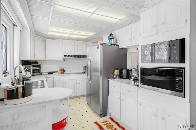 kitchen with sink, appliances with stainless steel finishes, white cabinetry, a drop ceiling, and decorative backsplash