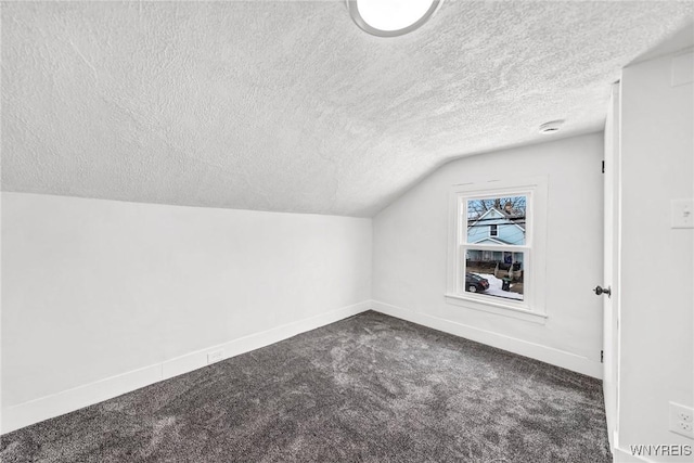 additional living space with lofted ceiling, a textured ceiling, and dark colored carpet