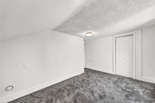 additional living space with vaulted ceiling, a textured ceiling, and dark colored carpet