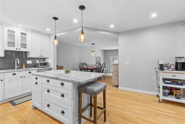 kitchen with a kitchen island, pendant lighting, white cabinetry, sink, and a breakfast bar area