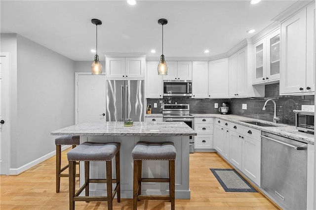 kitchen featuring appliances with stainless steel finishes, decorative light fixtures, sink, white cabinets, and a center island