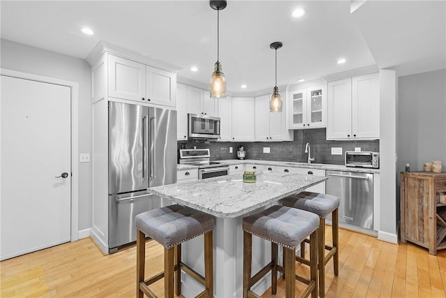 kitchen with a kitchen island, appliances with stainless steel finishes, pendant lighting, white cabinets, and a kitchen breakfast bar