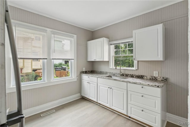 kitchen featuring light stone counters, sink, a wealth of natural light, and white cabinets