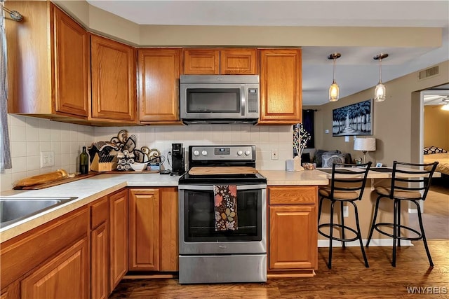 kitchen featuring visible vents, brown cabinets, dark wood-type flooring, appliances with stainless steel finishes, and light countertops