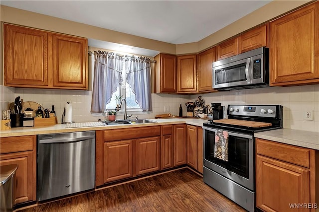 kitchen with a sink, light countertops, brown cabinets, appliances with stainless steel finishes, and dark wood-style flooring