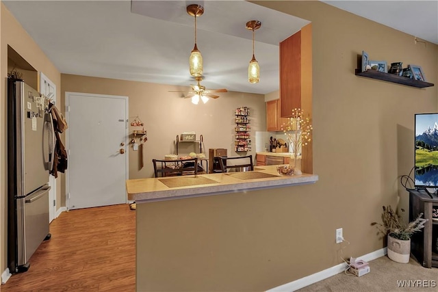 kitchen with freestanding refrigerator, a peninsula, baseboards, ceiling fan, and hanging light fixtures