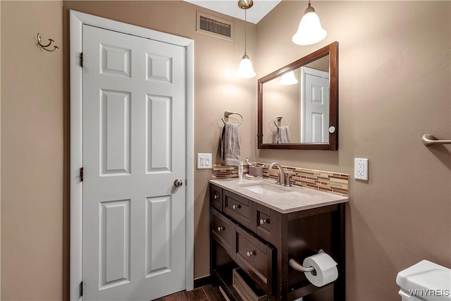 half bathroom with visible vents, vanity, decorative backsplash, and toilet