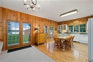 dining room with light wood-type flooring, an inviting chandelier, and wooden walls