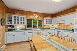 kitchen with light wood-type flooring, wooden walls, white electric range oven, and white cabinets