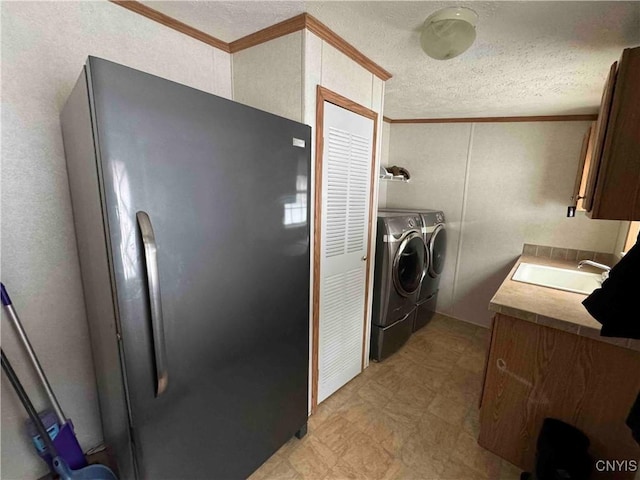 laundry area featuring crown molding, washing machine and clothes dryer, sink, and a textured ceiling