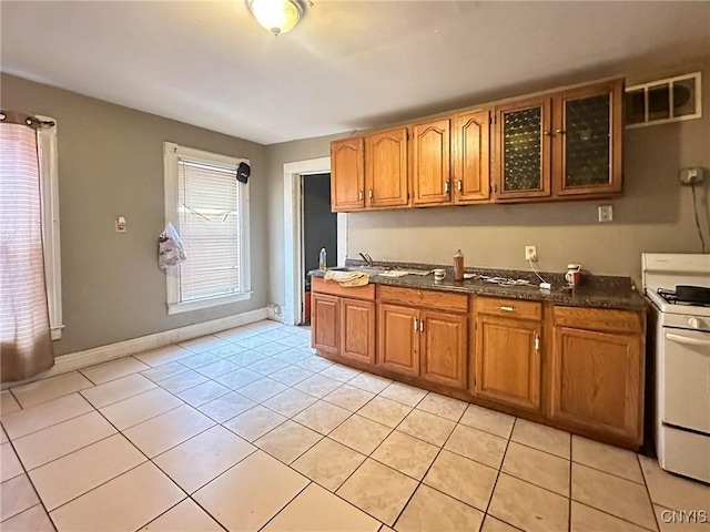 kitchen with light tile patterned floors, glass insert cabinets, brown cabinets, and white gas range oven
