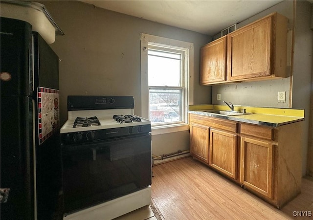 kitchen featuring light wood-style flooring, freestanding refrigerator, a sink, gas range, and brown cabinets