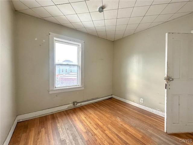 empty room featuring baseboards, a paneled ceiling, light wood-style floors, and a baseboard radiator