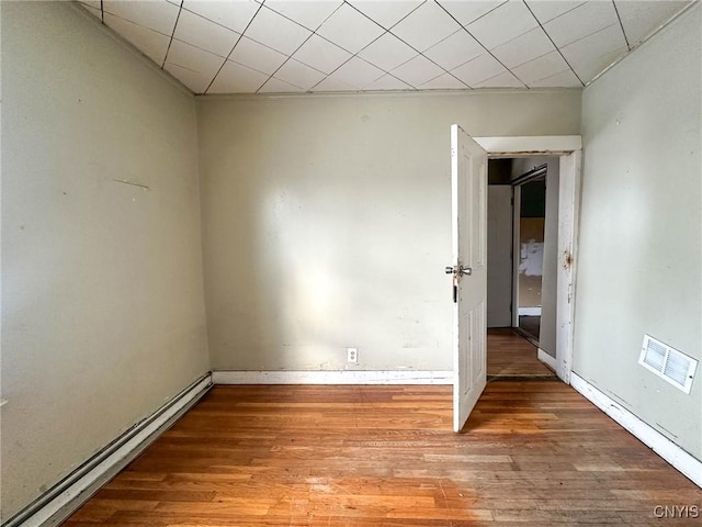 empty room with a baseboard radiator, visible vents, and wood finished floors