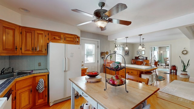 kitchen with sink, a center island, light hardwood / wood-style flooring, pendant lighting, and white appliances