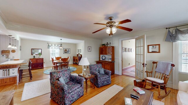 living room featuring ceiling fan, ornamental molding, a healthy amount of sunlight, and light wood-type flooring