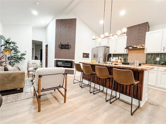 kitchen with decorative light fixtures, stainless steel fridge, an island with sink, white cabinets, and backsplash