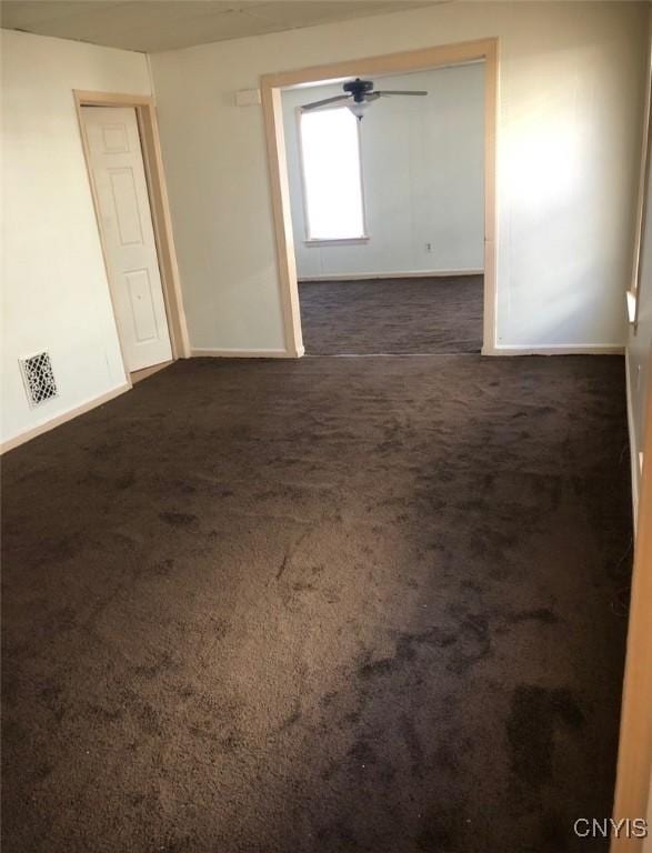 empty room with ceiling fan and dark colored carpet