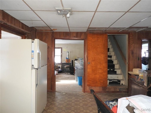 interior space with a drop ceiling, wooden walls, and white refrigerator