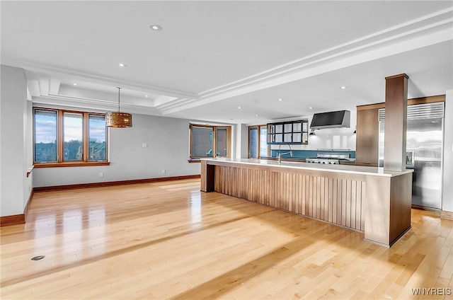 kitchen with a wealth of natural light, an island with sink, hanging light fixtures, and wall chimney range hood