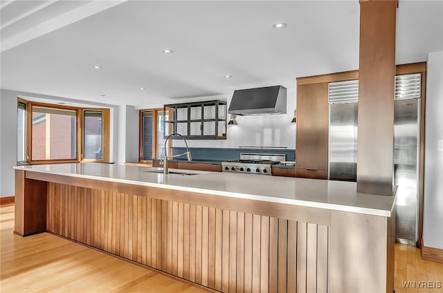 kitchen with sink, range, light wood-type flooring, and wall chimney exhaust hood