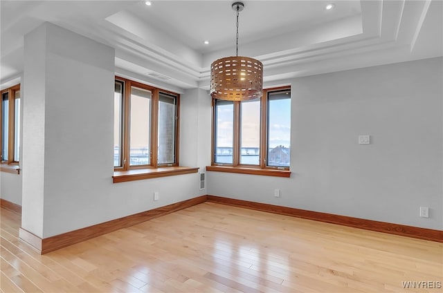 empty room featuring a tray ceiling and light wood-type flooring