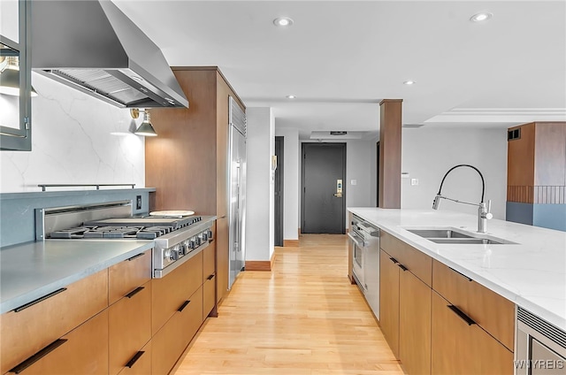 kitchen with ventilation hood, stainless steel gas stovetop, sink, light stone counters, and light wood-type flooring