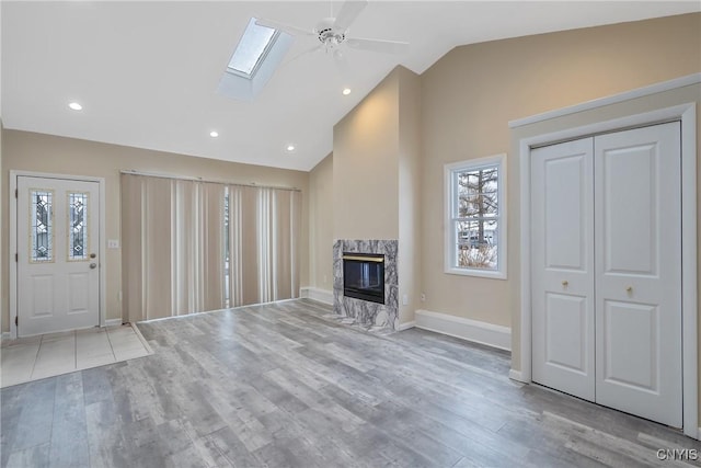 unfurnished living room featuring ceiling fan, a high end fireplace, vaulted ceiling with skylight, and light wood-type flooring