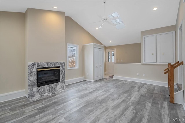 living room with ceiling fan, a skylight, high vaulted ceiling, a fireplace, and light wood-type flooring