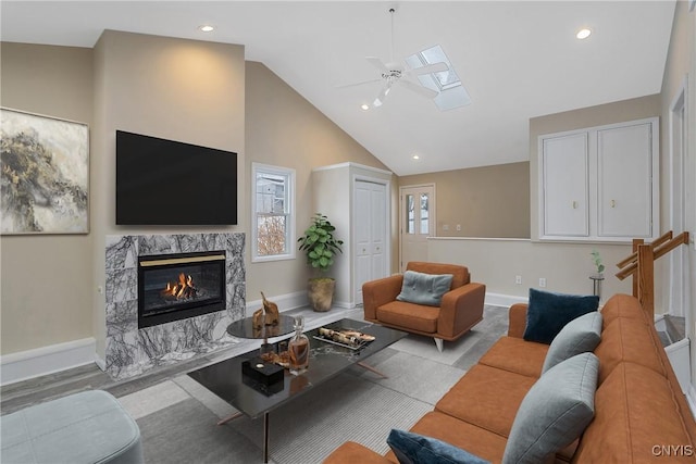 living room featuring ceiling fan, a high end fireplace, a skylight, and high vaulted ceiling