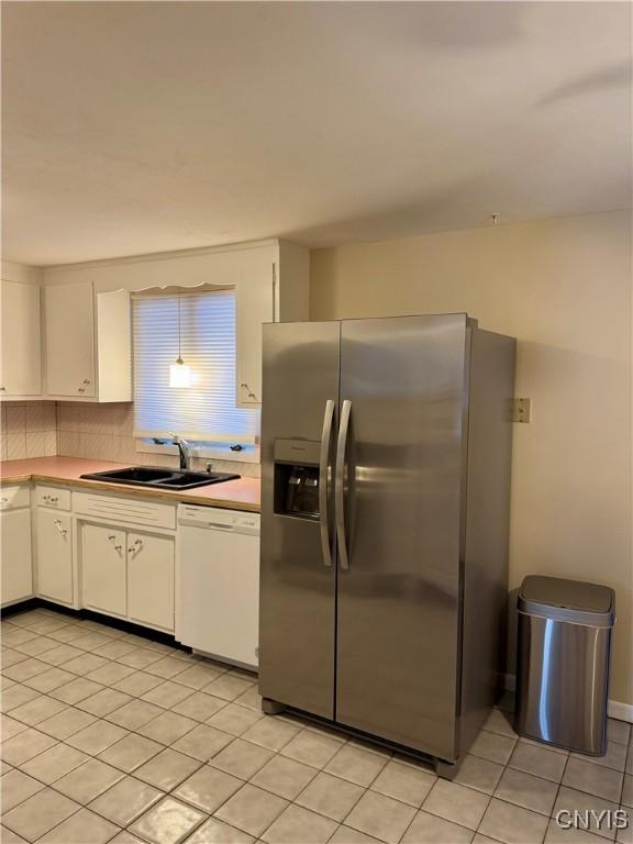 kitchen featuring dishwasher, sink, white cabinets, light tile patterned floors, and stainless steel refrigerator with ice dispenser