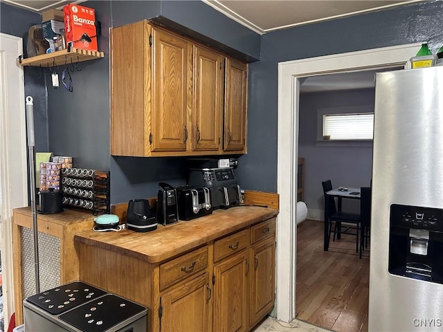 kitchen with wood finished floors, stainless steel fridge with ice dispenser, wooden counters, brown cabinets, and crown molding