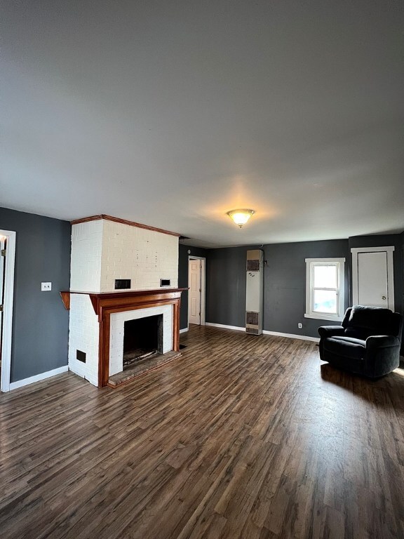 unfurnished living room featuring a brick fireplace and dark hardwood / wood-style floors