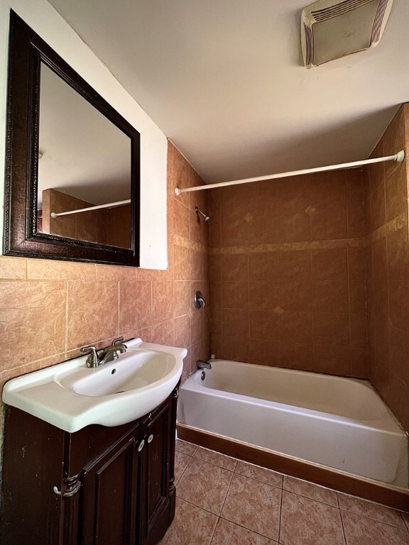 bathroom featuring tile walls, decorative backsplash, tiled shower / bath combo, vanity, and tile patterned floors