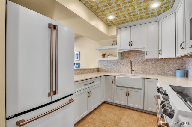 kitchen featuring high end fridge, sink, tasteful backsplash, stainless steel stove, and white cabinets