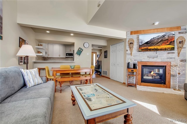 carpeted living room featuring a stone fireplace