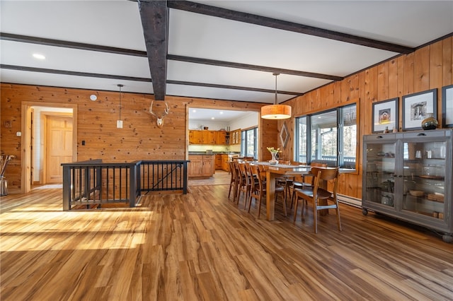 dining space featuring beam ceiling, light hardwood / wood-style flooring, and wooden walls