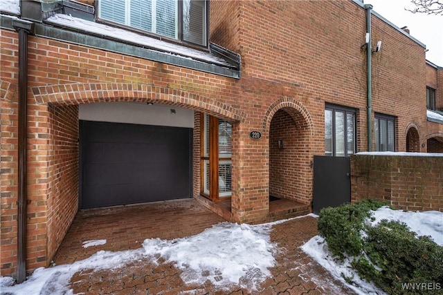 snow covered property entrance featuring a garage