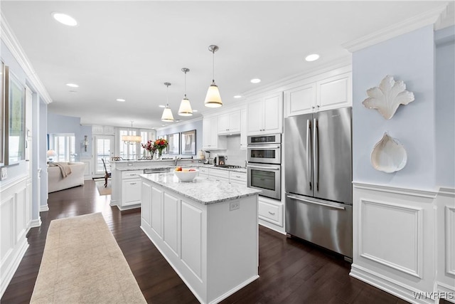 kitchen with light stone counters, appliances with stainless steel finishes, a kitchen island, pendant lighting, and white cabinets