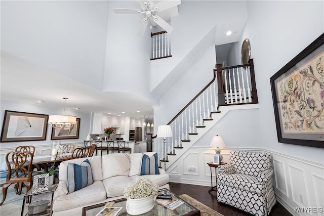 living room featuring dark hardwood / wood-style flooring, ceiling fan with notable chandelier, and a high ceiling