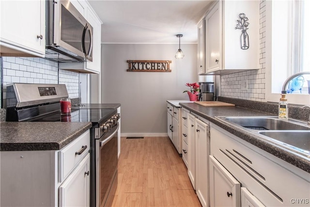 kitchen featuring stainless steel appliances, sink, white cabinets, and decorative light fixtures