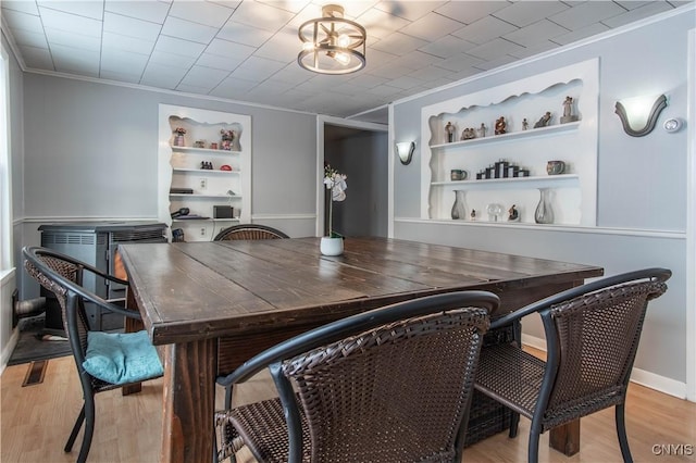 dining room featuring crown molding, built in shelves, an inviting chandelier, and light hardwood / wood-style flooring