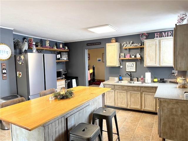 kitchen featuring wood counters, sink, a breakfast bar area, light brown cabinets, and stainless steel refrigerator