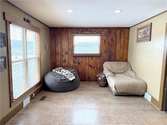 living area with crown molding, a wealth of natural light, and wooden walls