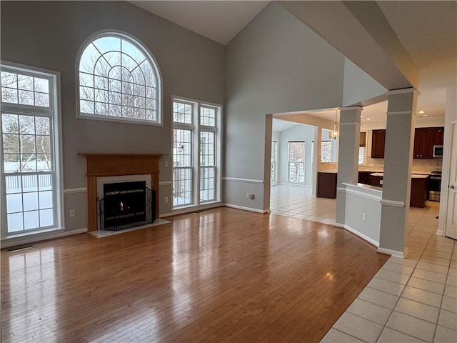 unfurnished living room featuring a high ceiling, a high end fireplace, decorative columns, and light hardwood / wood-style floors