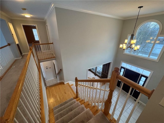 stairs featuring a high ceiling, ornamental molding, hardwood / wood-style floors, and a notable chandelier